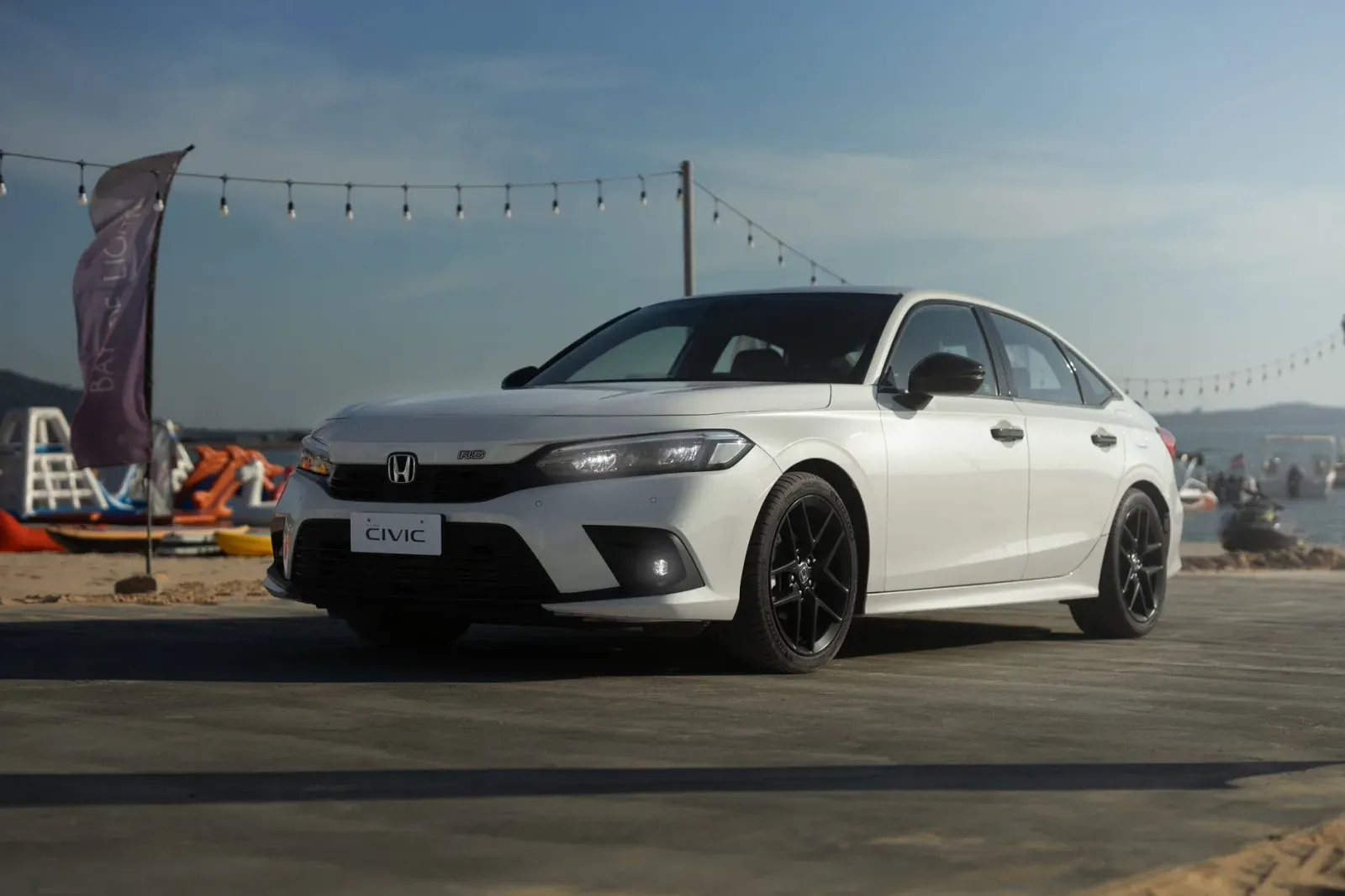 Beyaz Honda Civic sedan, ön çamurluk üzerinde "CIVIC" yazısı ve Honda logosu net görünüyor, açık havada plaj kenarında park hâlinde