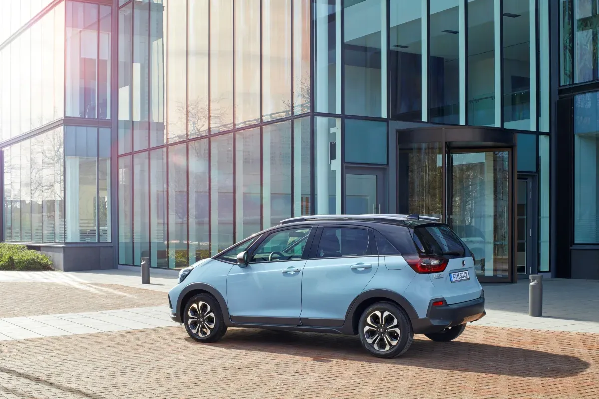 Açık mavi Honda Jazz hatchback, cam cepheli bir bina önünde arka çapraz açı, kaportada "JAZZ" yazısı net okunuyor